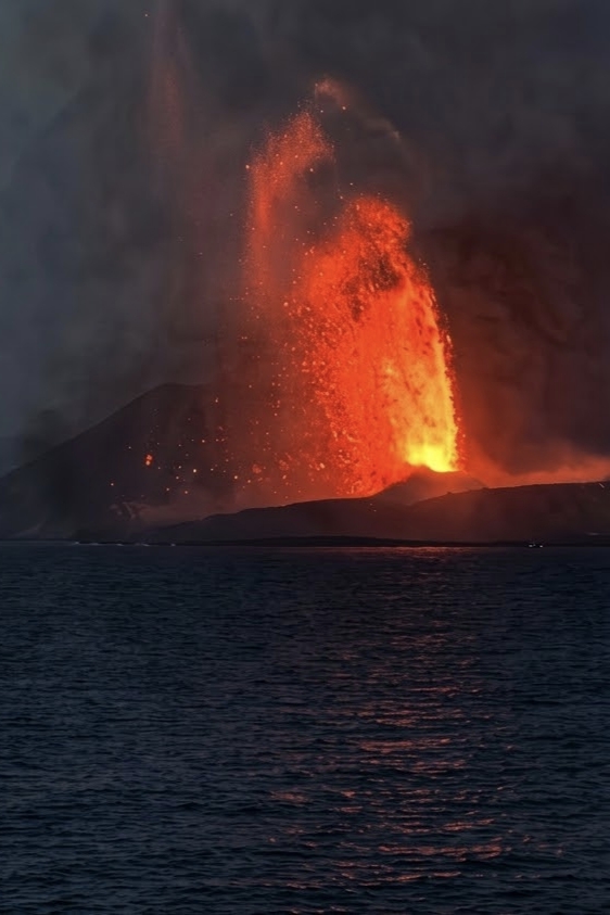 Anak Krakatau volcano erupting at night with a fountain of glowing lava and a tall dark ash column, photographed from the water in the Sunda Strait on 5 September 2026.
