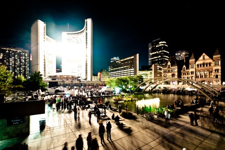 Crowds filling Nathan Phillips Square at night with Toronto City Hall lit behind them during Nuit Blanche