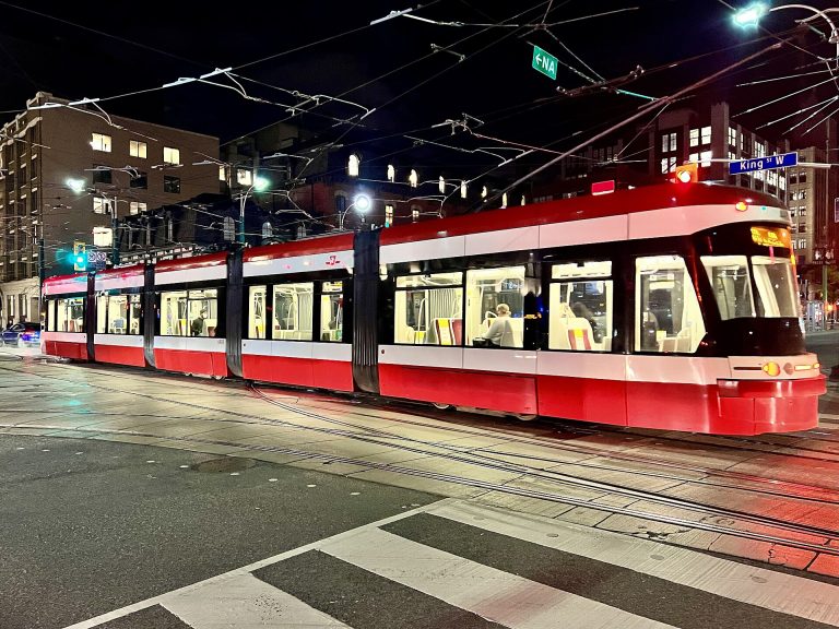 A Flexity Outlook streetcar at Spadina Avenue and King Street West at night
