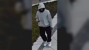 A man in a grey hooded sweatshirt, black pants and white shoes walking on a sidewalk
