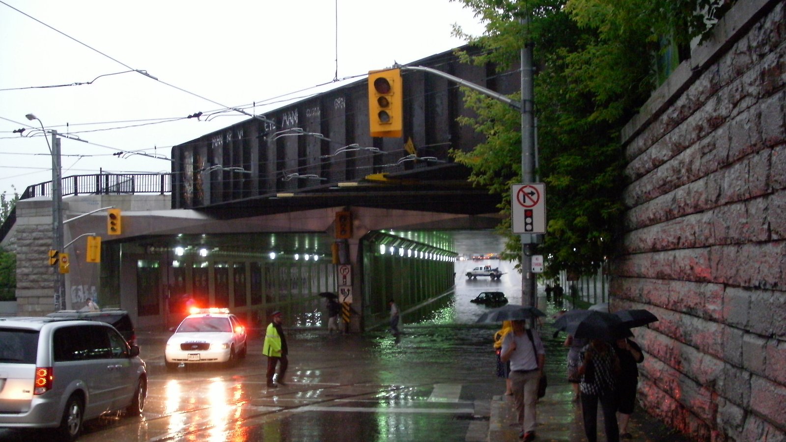 A flooded road underpass in Toronto with a car driving through standing water