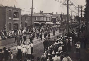 Black and white photograph of a Labour Day parade marching east along Queen Street West in Toronto in 1905, with crowds lining the street.