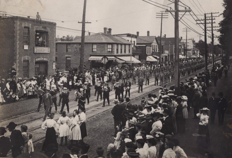 Black and white photograph of a Labour Day parade marching east along Queen Street West in Toronto in 1905, with crowds lining the street.