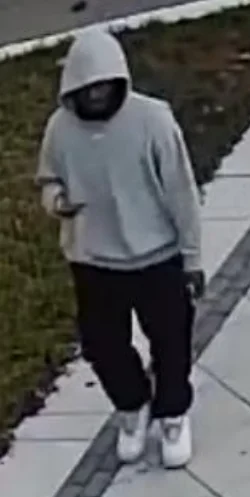 A man in a grey hooded sweatshirt, black pants and white shoes walking on a sidewalk